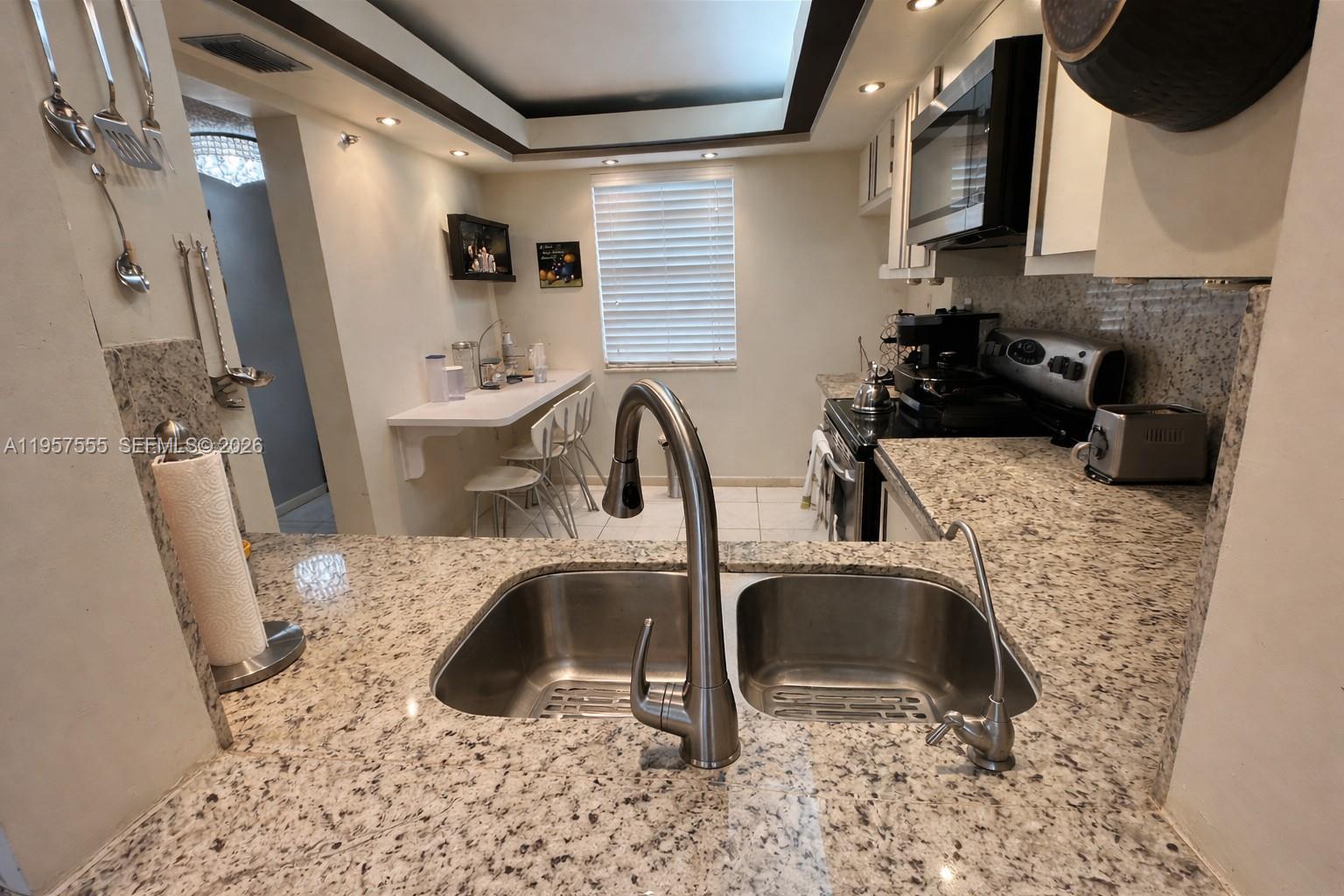 A kitchen features granite countertops, a double-basin sink, and a small breakfast bar area — 3910 Inverrary Blvd # B, Lauderhill FL 33319, LAUDERHILL, FL