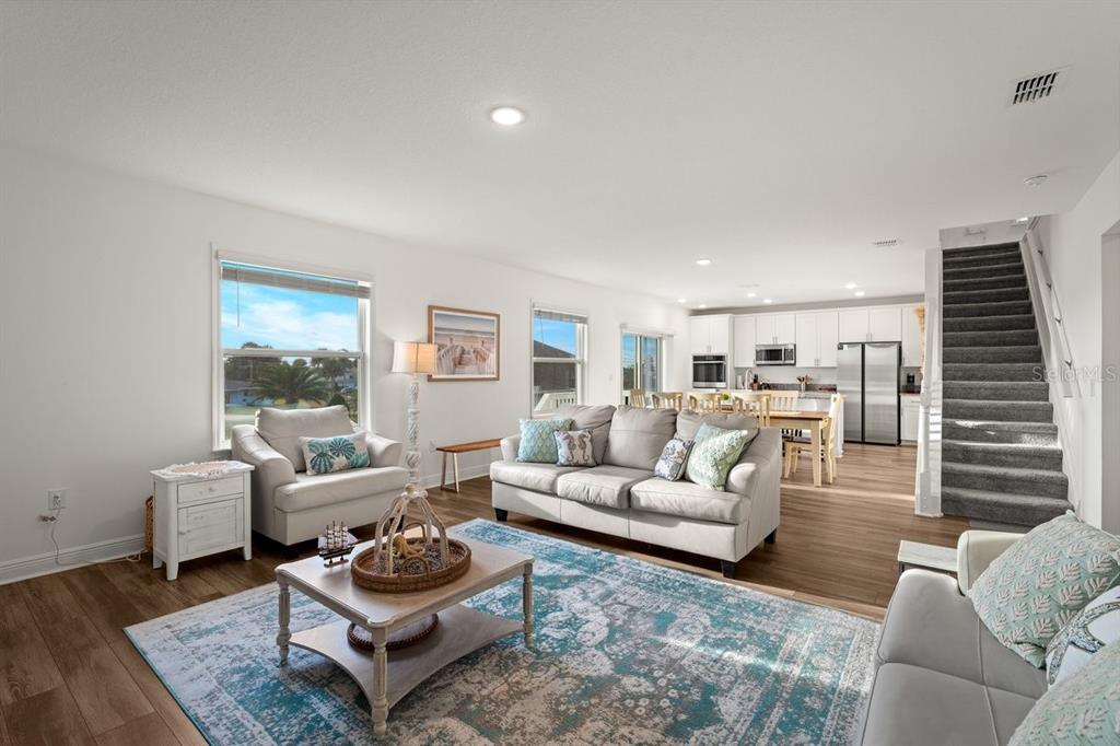 An open-concept living room and kitchen with light wood flooring, neutral furniture, and carpeted stairs — 3828 S ATLANTIC AVENUE, DAYTONA BEACH SHORES, FL