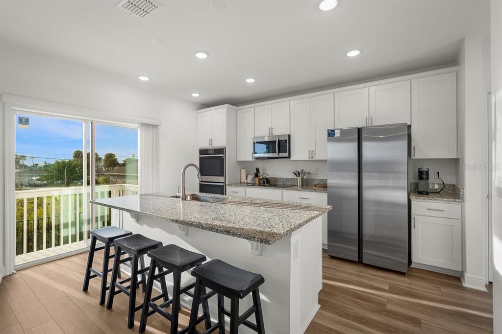 A modern kitchen features white cabinets, granite countertops, stainless steel appliances, and a breakfast island — 3828 S ATLANTIC AVENUE, DAYTONA BEACH SHORES, FL
