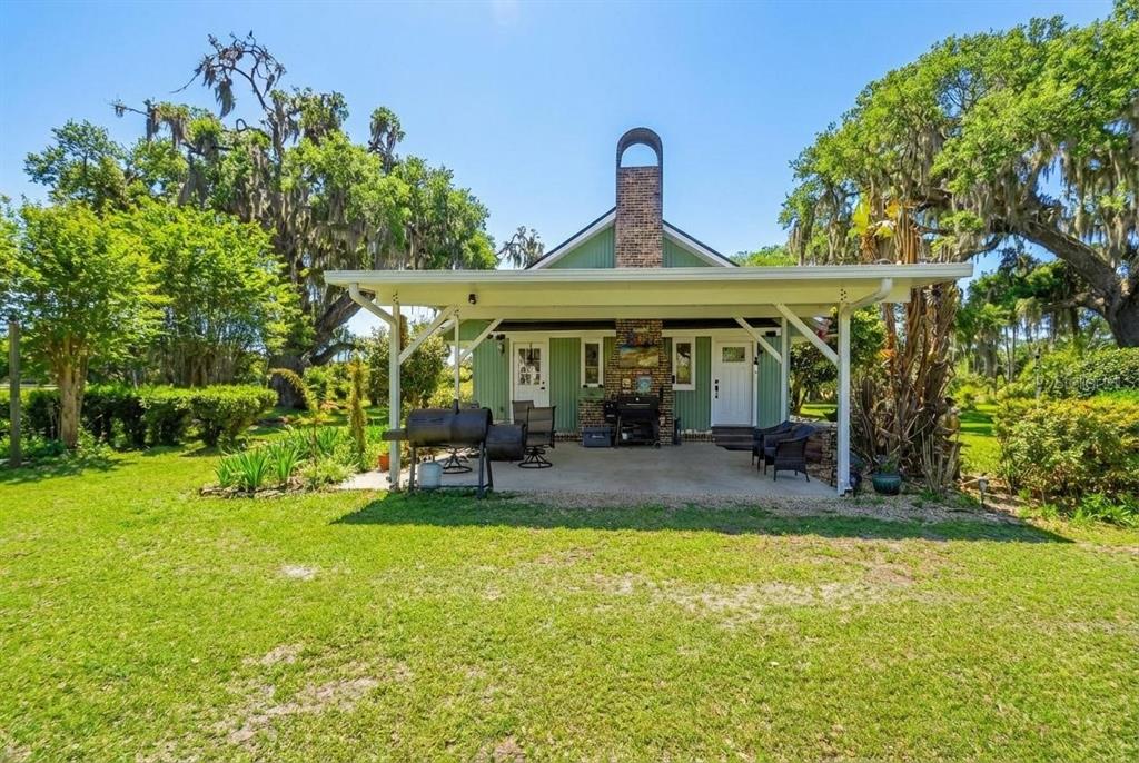 A green house with a brick chimney and a covered patio sits on a lawn — 1403 BLACKWELDER ROAD, DE LEON SPRINGS, FL