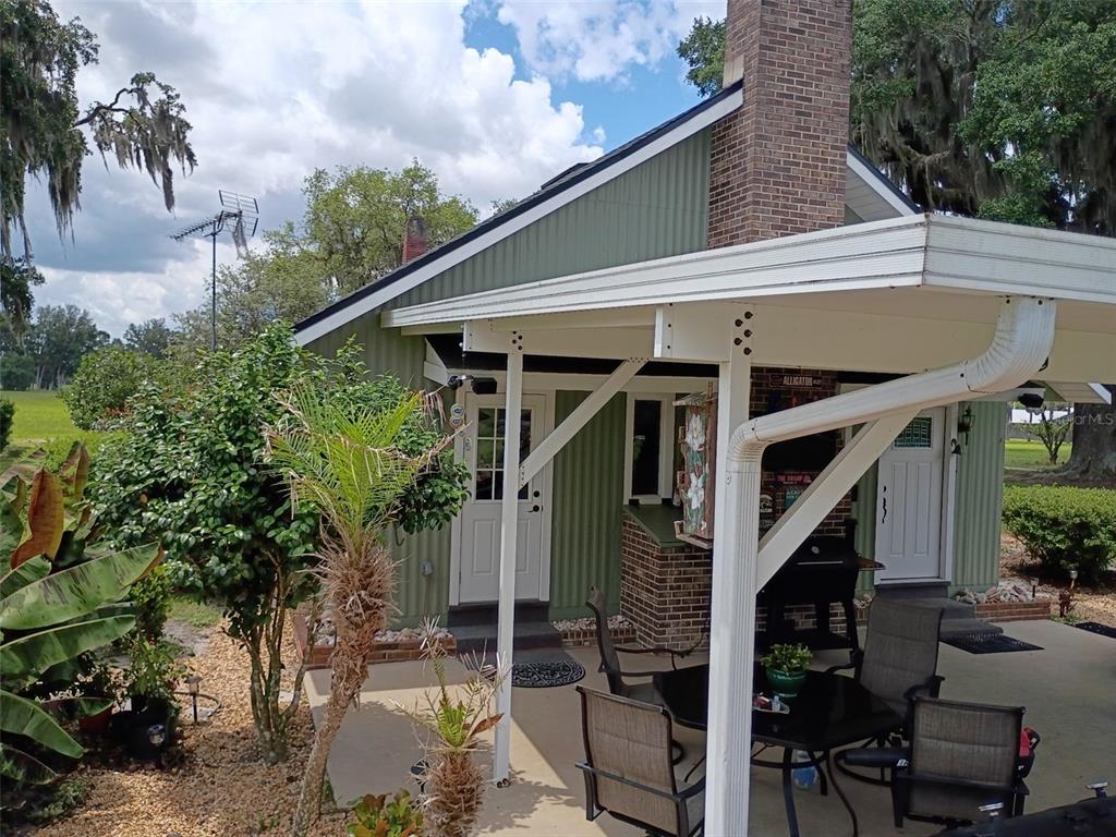 A green metal-sided house with a brick chimney and a covered patio with outdoor furniture — 1403 BLACKWELDER ROAD, DE LEON SPRINGS, FL