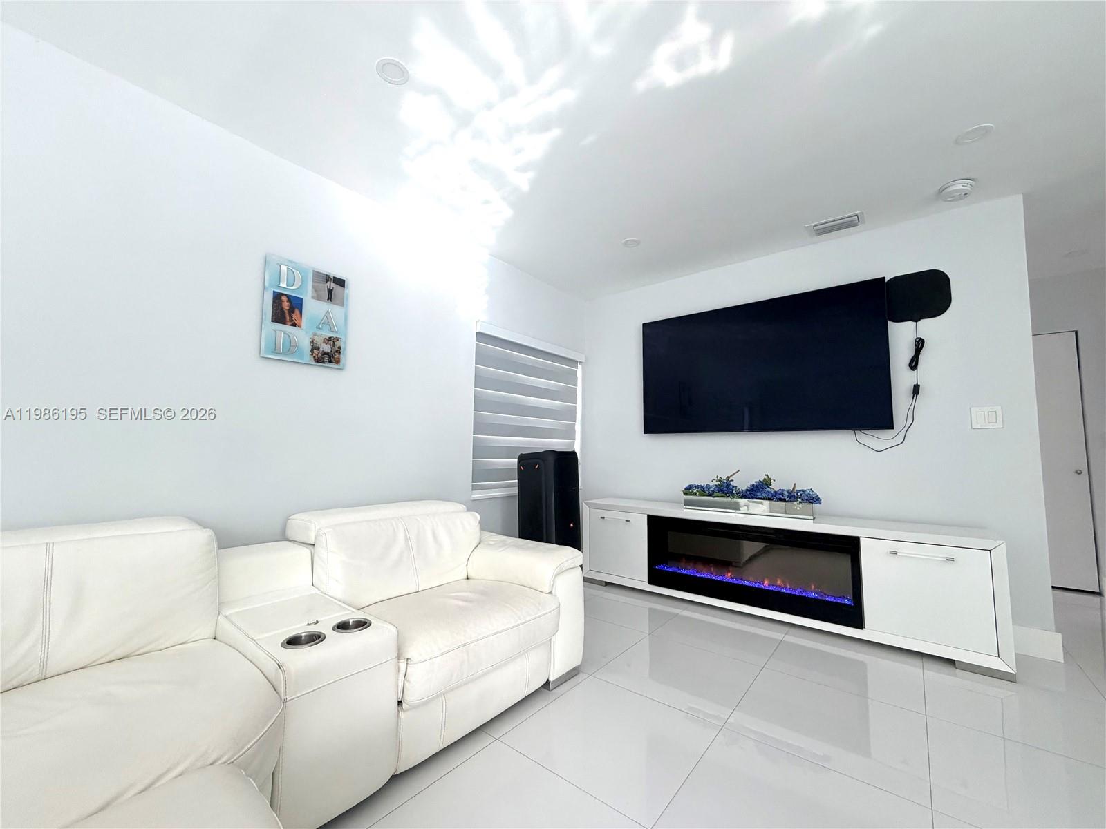 A living room features a white leather sectional, a wall-mounted television, and an electric fireplace — 14401 Boggs Dr, Miami FL 33176, MIAMI, FL
