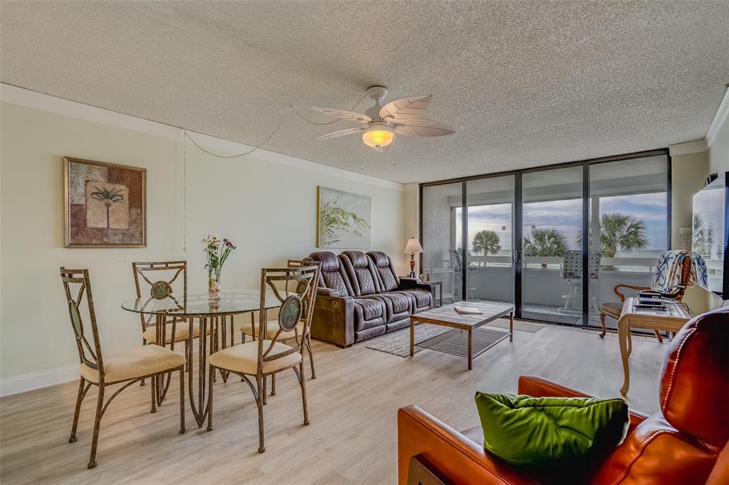 A living and dining area with light wood floors, a ceiling fan, and sliding glass doors — 17900 GULF BOULEVARD UNIT 2E, REDINGTON SHORES, FL