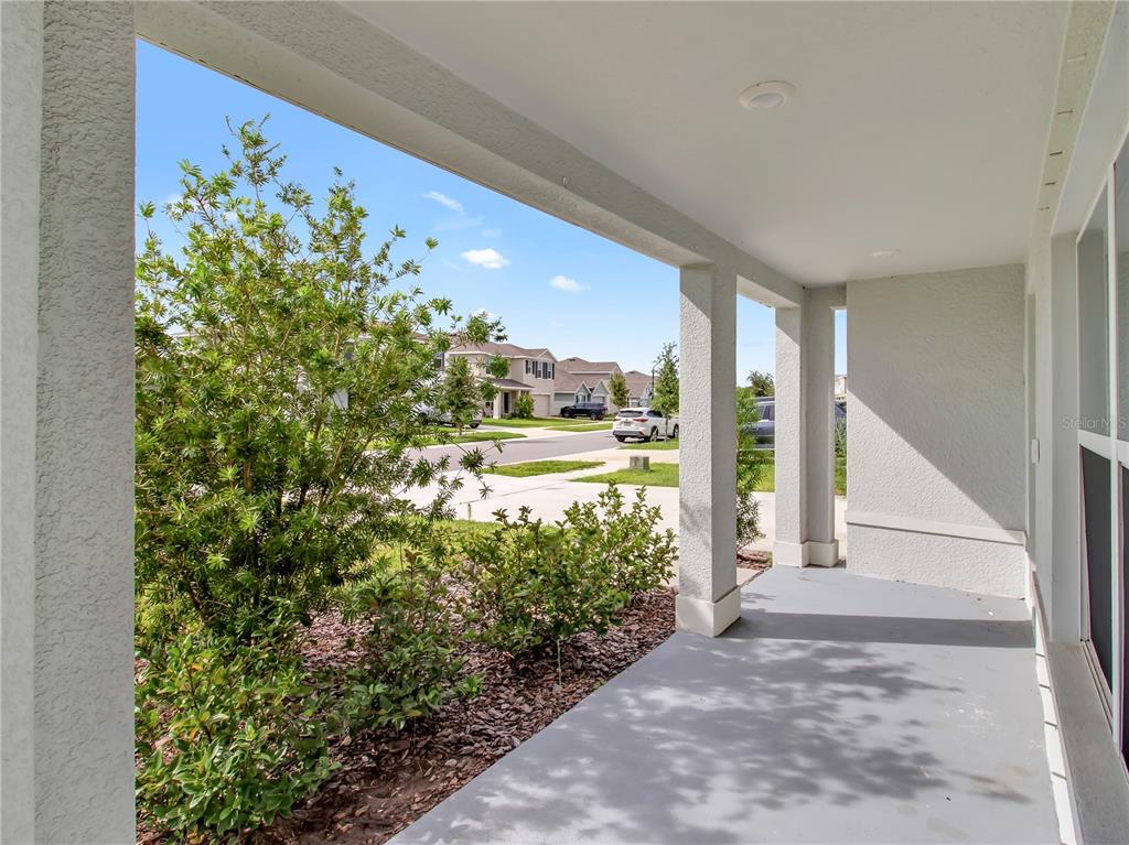 A covered concrete porch overlooks a suburban street with houses and parked cars — 16523 WINDMILL FORGE PASS, WIMAUMA, FL