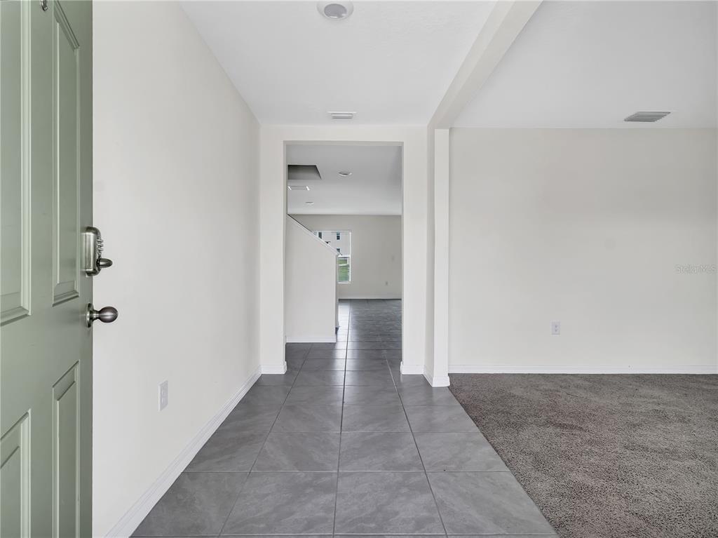 An entryway with gray tile flooring leads to a carpeted living area and hallway — 16523 WINDMILL FORGE PASS, WIMAUMA, FL