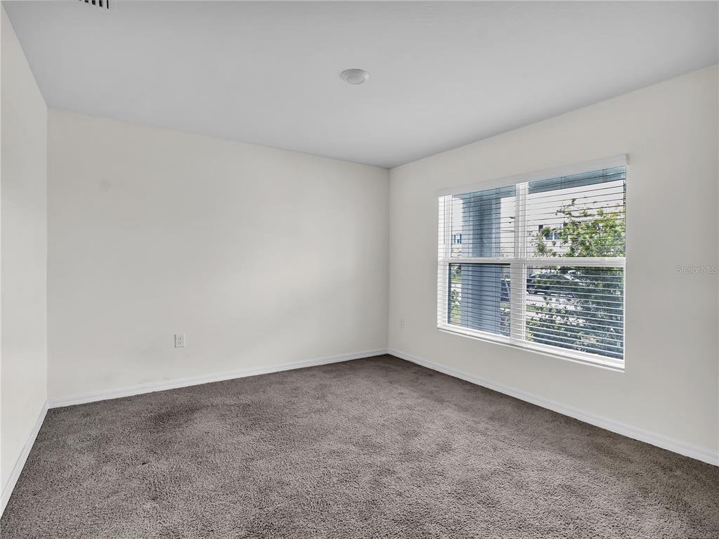 An empty bedroom features beige walls, gray carpeting, and a window with white blinds — 16523 WINDMILL FORGE PASS, WIMAUMA, FL