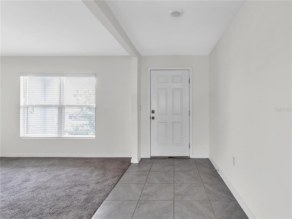 A room with a gray tiled entryway, carpeted flooring, a white door, and a window — 16523 WINDMILL FORGE PASS, WIMAUMA, FL