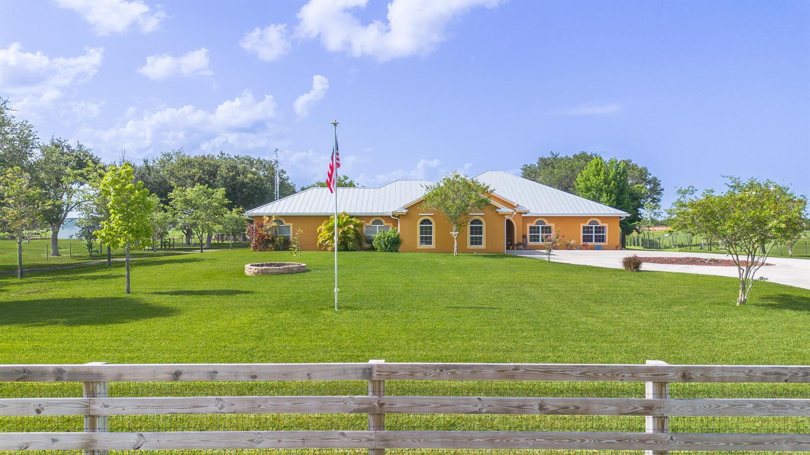 A single-story orange house with a metal roof sits behind a wooden fence — 7611 SW 21st Parkway, Okeechobee FL 34974, OKEECHOBEE, FL