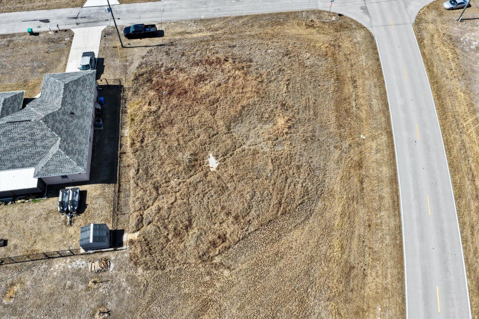An aerial view shows a vacant, dry grass lot situated next to a residential house — Blk 34 Naples Street, FL 33935, FL