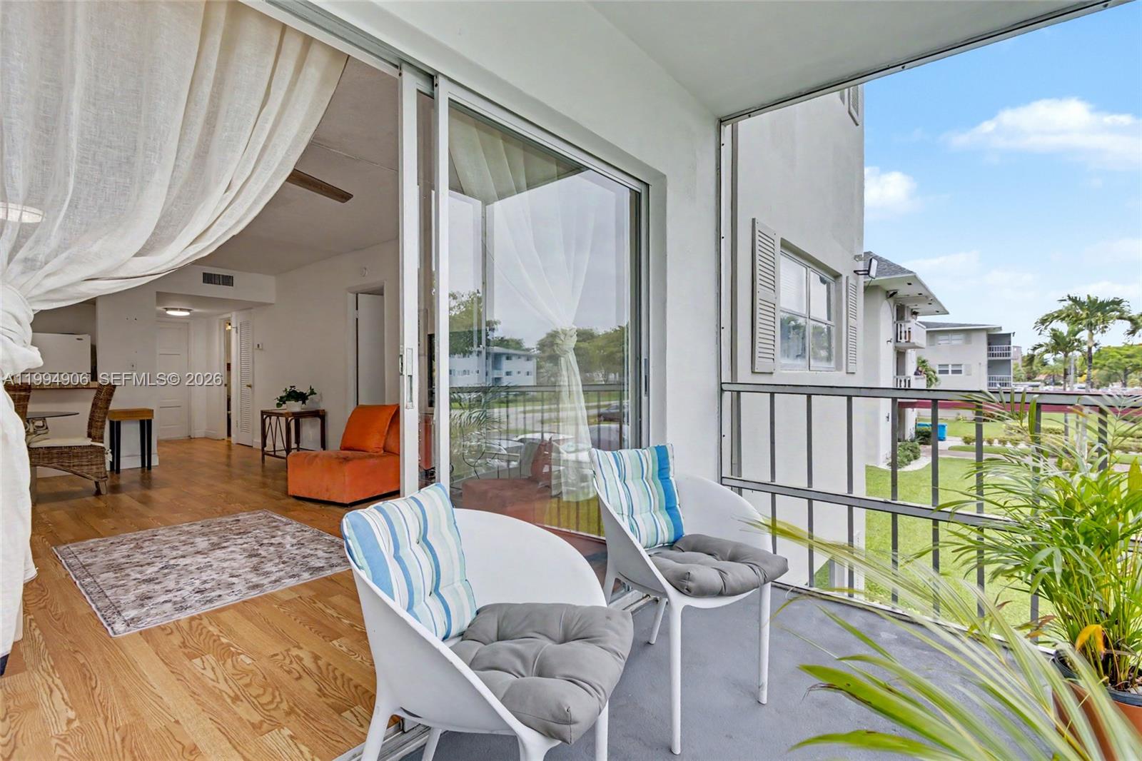 A balcony with two white chairs overlooks a grassy area next to an interior room — 1000 Hillcrest Ct # 215, Hollywood FL 33021, HOLLYWOOD, FL