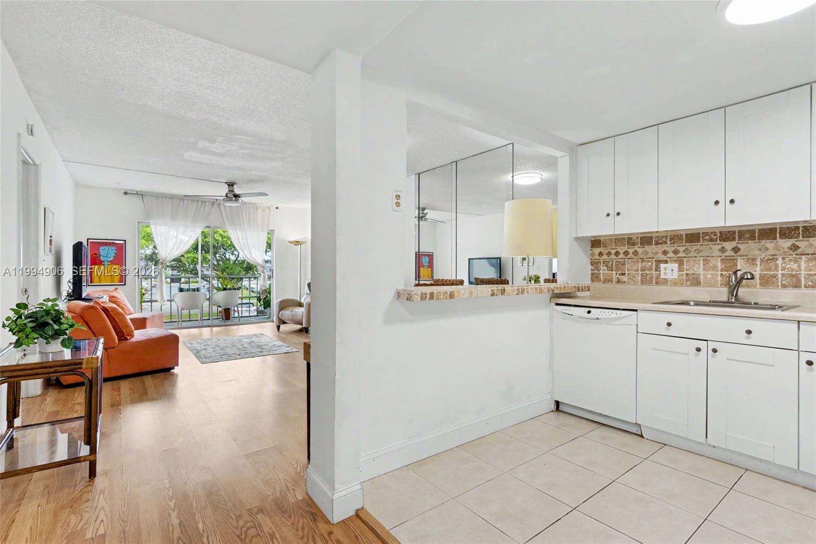 A kitchen with white cabinets and tile flooring opens to a living room with wood floors — 1000 Hillcrest Ct # 215, Hollywood FL 33021, HOLLYWOOD, FL