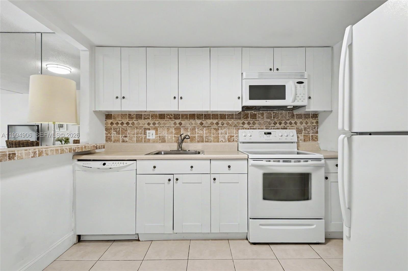 A kitchen features white cabinetry, a tiled backsplash, white appliances, and a beige countertop — 1000 Hillcrest Ct # 215, Hollywood FL 33021, HOLLYWOOD, FL
