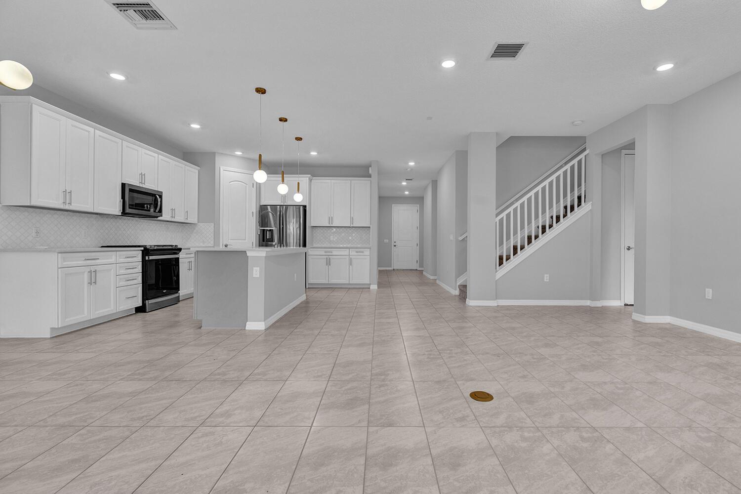 A bright, open-concept kitchen features white cabinetry, a central island, and light-colored tile flooring — 8296 Vaulting Drive, Lake Worth FL 33467, LAKE WORTH, FL