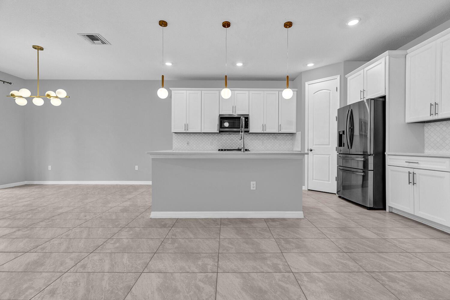 A modern kitchen features white cabinetry, stainless steel appliances, and a central island with pendants — 8296 Vaulting Drive, Lake Worth FL 33467, LAKE WORTH, FL