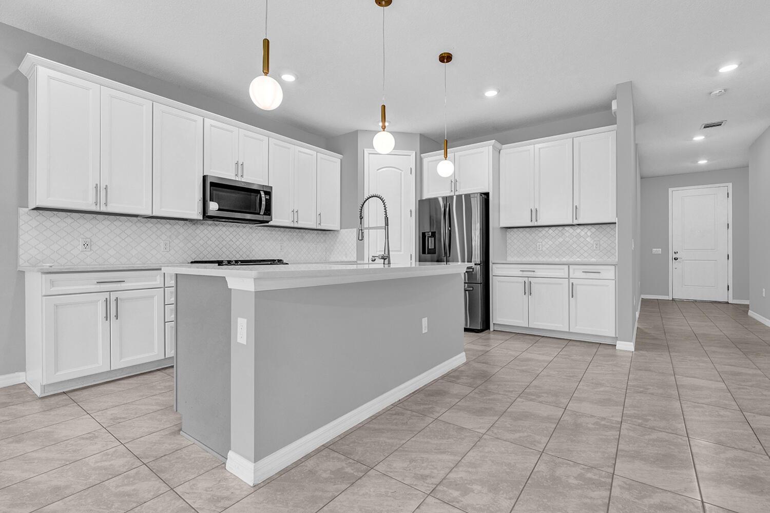 A modern kitchen features white cabinets, stainless steel appliances, a gray island, and tile flooring — 8296 Vaulting Drive, Lake Worth FL 33467, LAKE WORTH, FL
