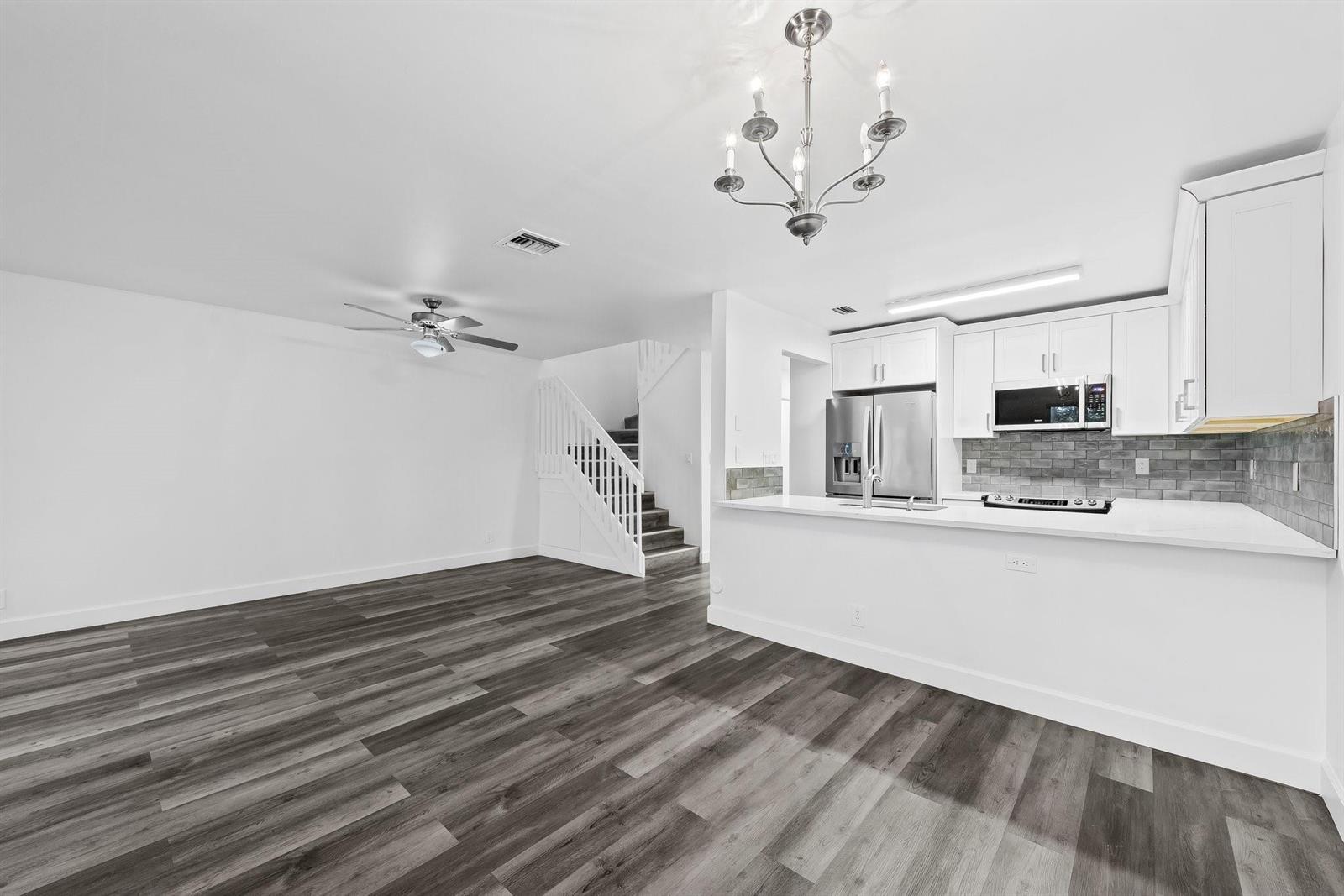 An open-concept kitchen and living area featuring white cabinets, stainless appliances, and gray wood flooring — 822 Crystal Lake Drive # 822, Deerfield Beach FL 33064, DEERFIELD BEACH, FL