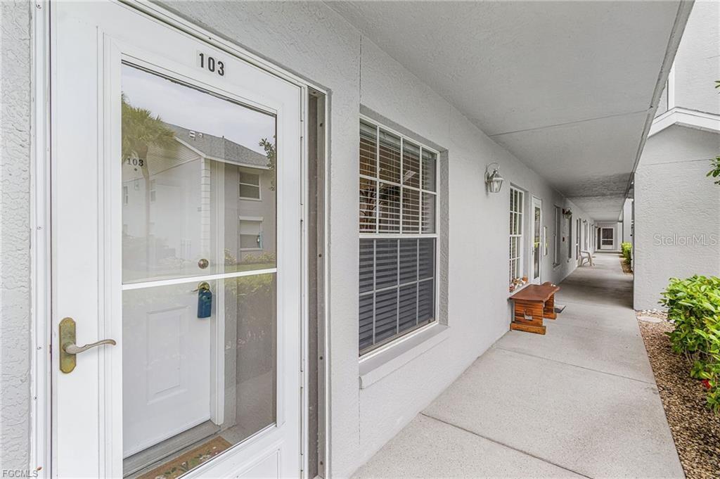 A white exterior walkway leads past apartment doors with glass storm doors and windows — 14461 LAKEWOOD TRACE COURT UNIT 103, FORT MYERS, FL