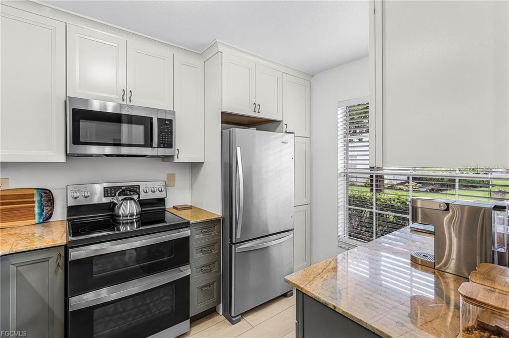 A kitchen features stainless steel appliances, white upper cabinets, dark lower cabinets, and granite countertops — 14461 LAKEWOOD TRACE COURT UNIT 103, FORT MYERS, FL
