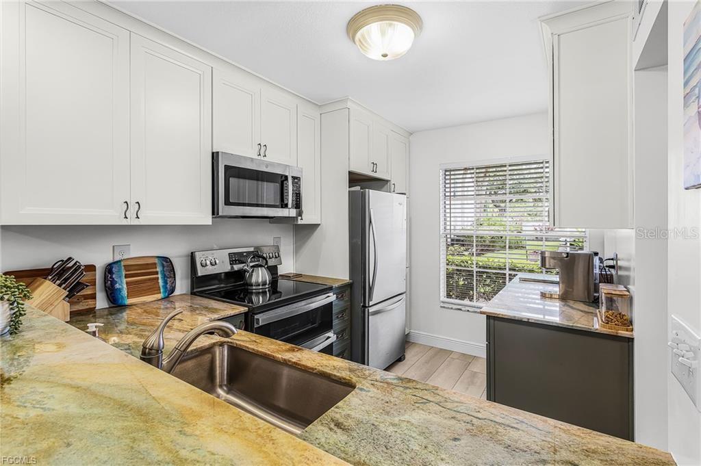 A kitchen features white cabinets, stainless steel appliances, and granite countertops with a sink — 14461 LAKEWOOD TRACE COURT UNIT 103, FORT MYERS, FL