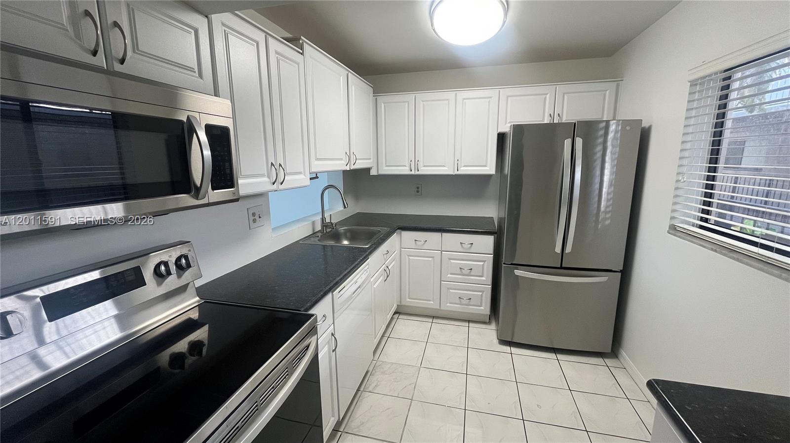A kitchen features white cabinets, stainless steel appliances, black countertops, and light-colored tile flooring — 8540 SW 133rd Ave Rd # 316, Miami FL 33183, MIAMI, FL