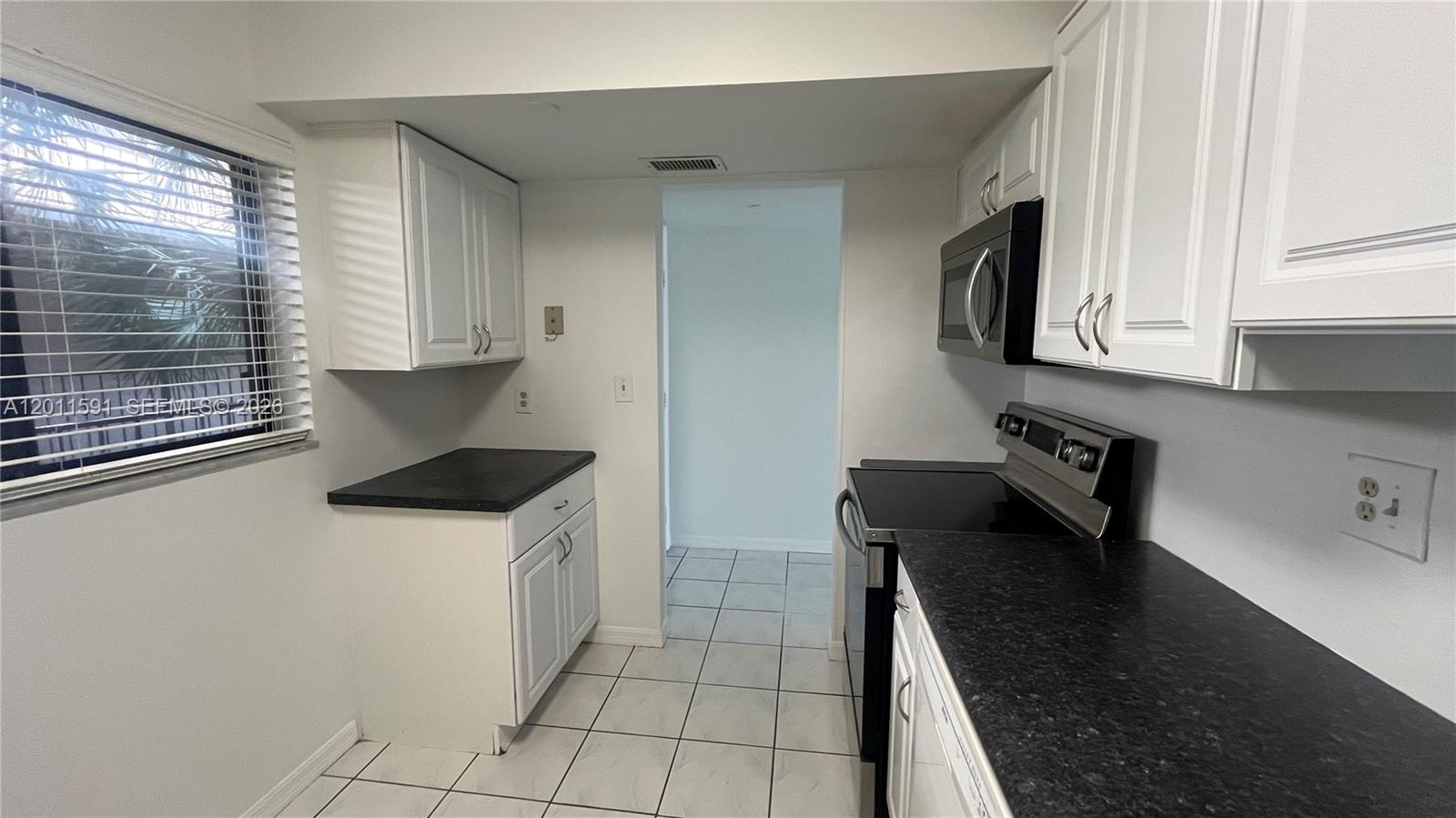 A kitchen features white cabinets, black countertops, stainless steel appliances, and white tile flooring — 8540 SW 133rd Ave Rd # 316, Miami FL 33183, MIAMI, FL