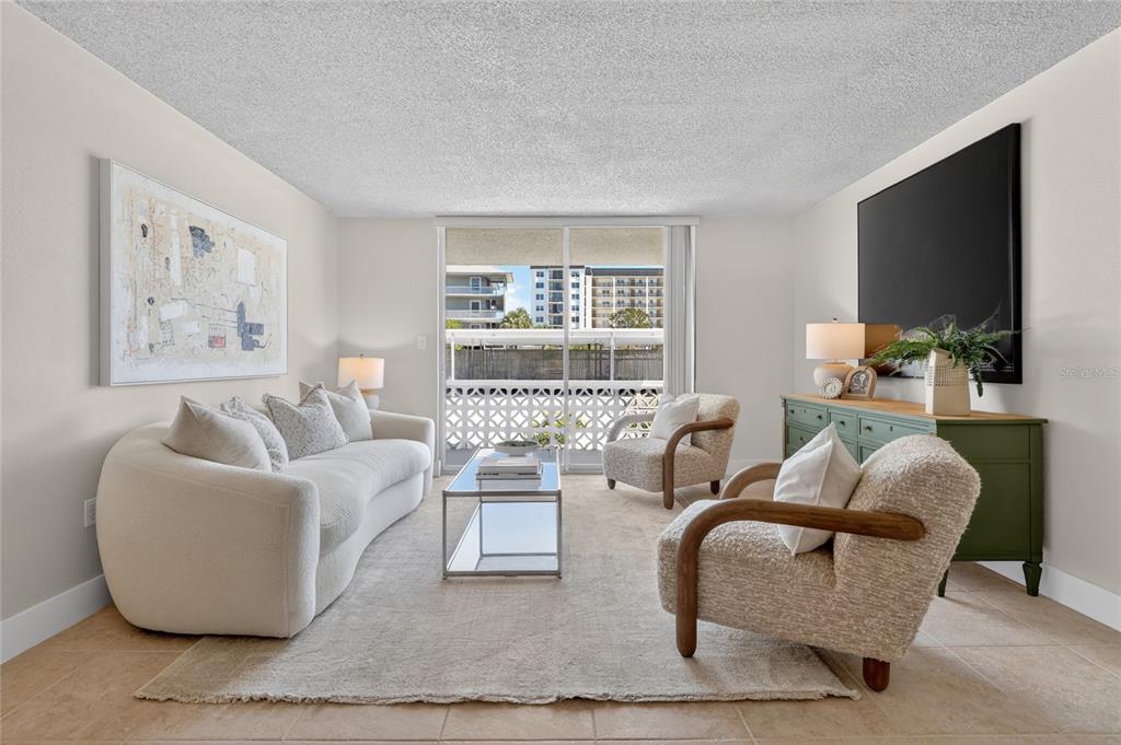 A living room features a curved white sofa, two armchairs, and a sliding glass door — 9 FORBES PLACE PLACE UNIT 112, DUNEDIN, FL