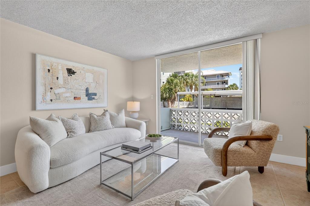 A living room features a white sofa, glass coffee table, armchair, and a sliding glass door — 9 FORBES PLACE PLACE UNIT 112, DUNEDIN, FL