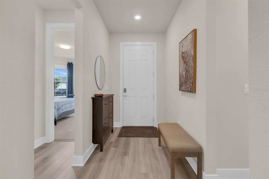 A bright entryway features light wood-look flooring, a white front door, and a wooden bench — 13031 SKYWAY LANE, ORLANDO, FL