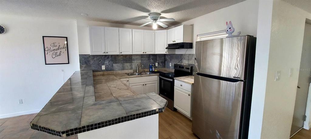 A kitchen features white cabinets, a tiled countertop, and stainless steel appliances — 2625 STATE ROAD 590 UNIT 2721, CLEARWATER, FL