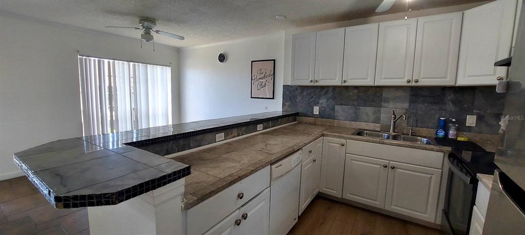 A kitchen features white cabinets, tiled countertops, a breakfast bar, and a slate backsplash — 2625 STATE ROAD 590 UNIT 2721, CLEARWATER, FL