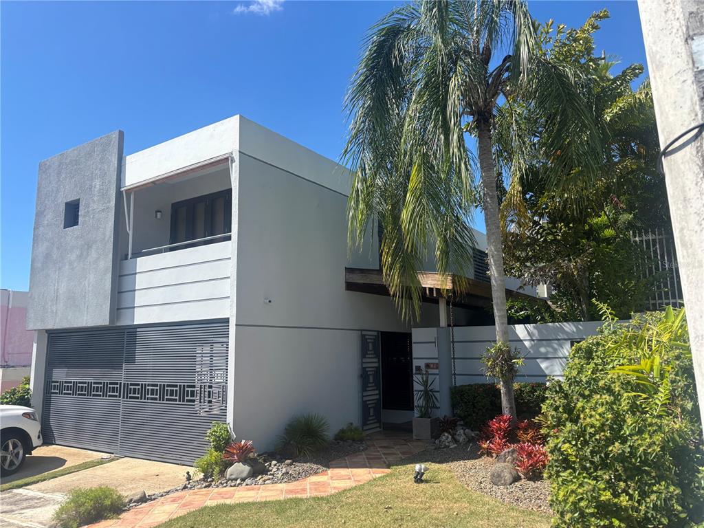 A two-story modern house features a gray facade, a slatted garage door, and a palm tree — W 4-14 CALDERÓN DE LA BARCA, SAN JUAN, PR