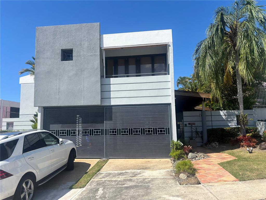 A two-story modern house features a gray textured facade, a large metal gate, and a balcony — W 4-14 CALDERÓN DE LA BARCA, SAN JUAN, PR