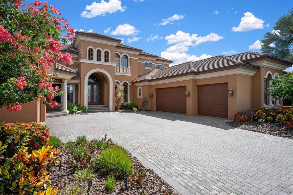 A two-story tan stucco house features a paved driveway, a three-car garage, and landscaping — 14115 11TH TERRACE NE, BRADENTON, FL