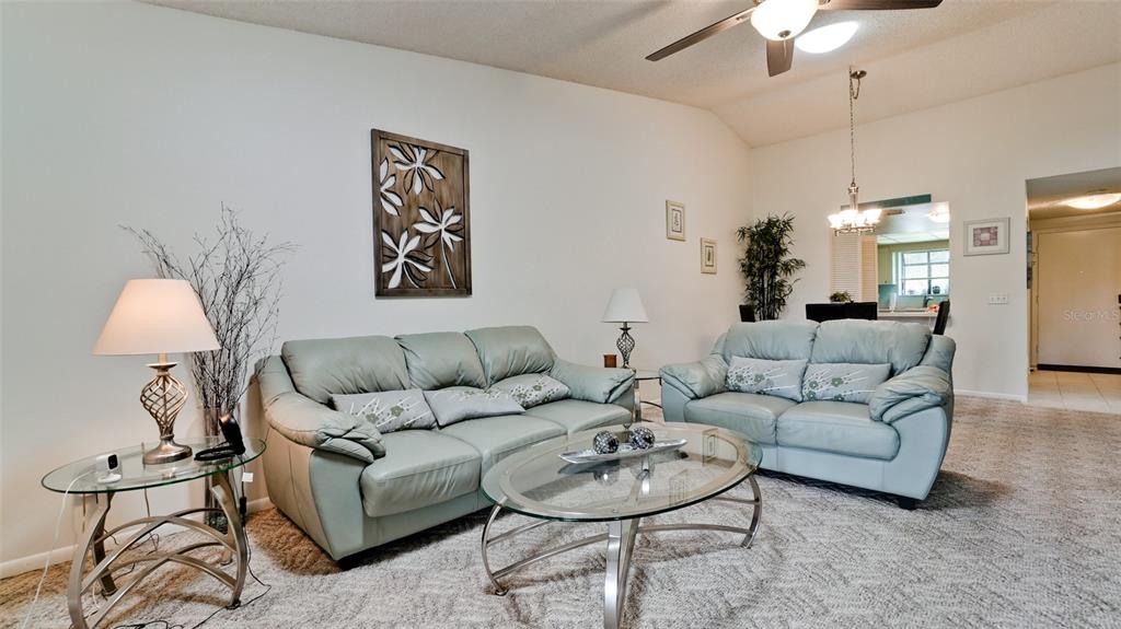 A living room features a light green leather sofa, glass coffee table, and sliding glass doors — 6507 HERITAGE LANE UNIT 2605, BRADENTON, FL