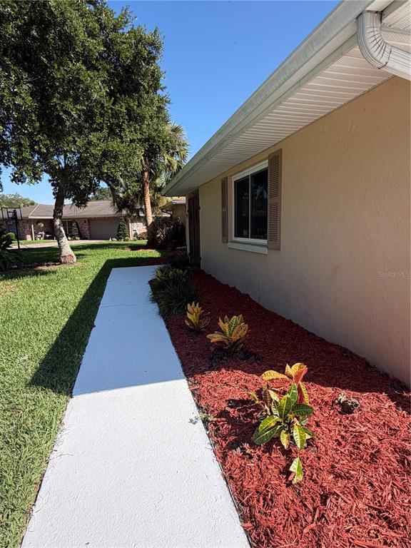 A concrete walkway leads along the side of a tan house with red mulch landscaping — 41 GREENFIELD COURT, WINTER HAVEN, FL
