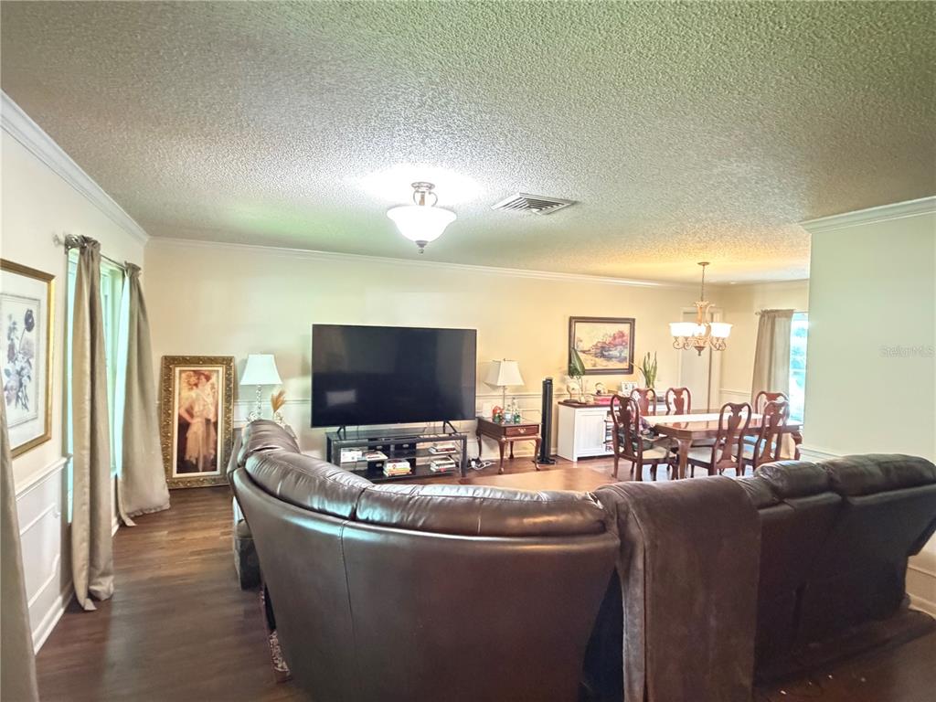 A living room with a large brown sectional sofa, a television, and an adjacent dining area — 41 GREENFIELD COURT, WINTER HAVEN, FL