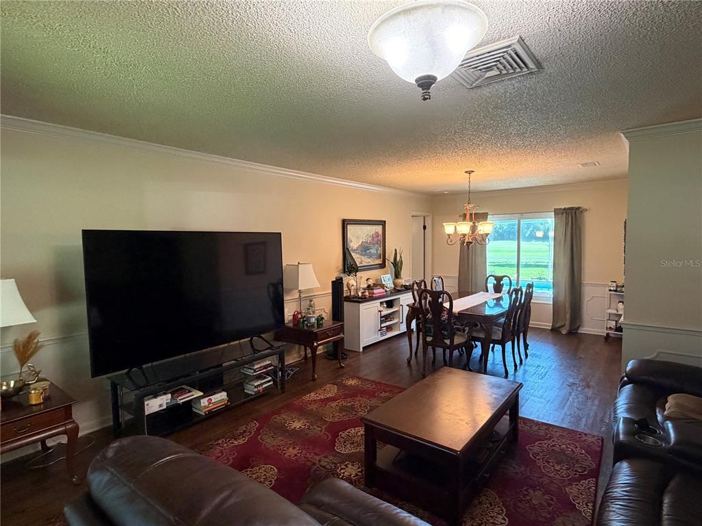 A living and dining area features dark wood flooring, a large television, and a chandelier — 41 GREENFIELD COURT, WINTER HAVEN, FL