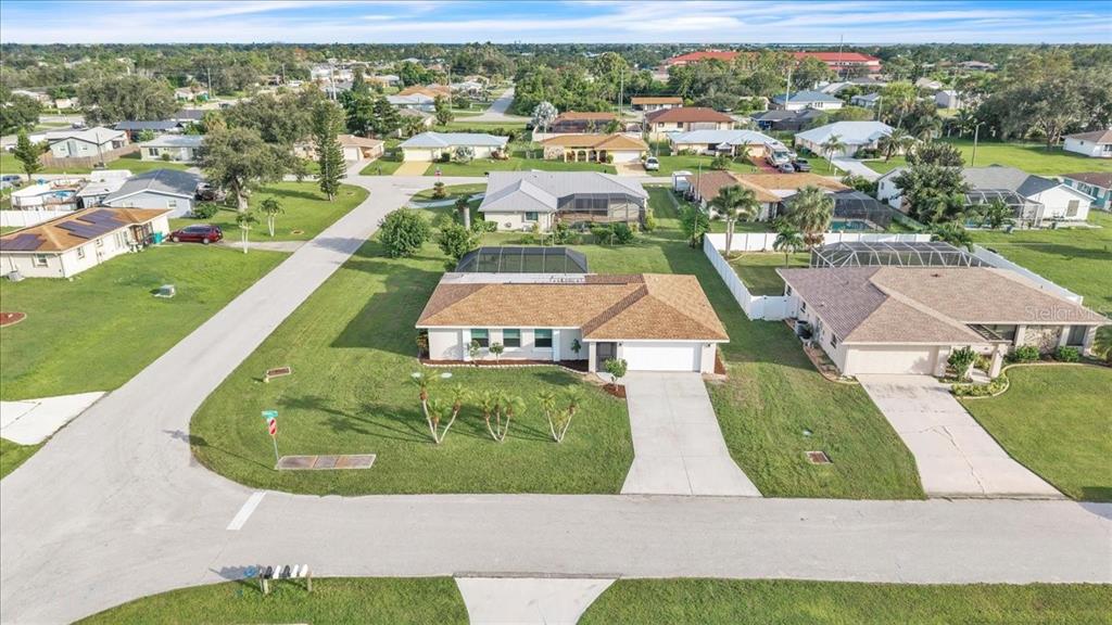 An aerial view shows a suburban house with a tan roof, pool enclosure, and driveway — 907 SIDNEY TERRACE NW, PORT CHARLOTTE, FL