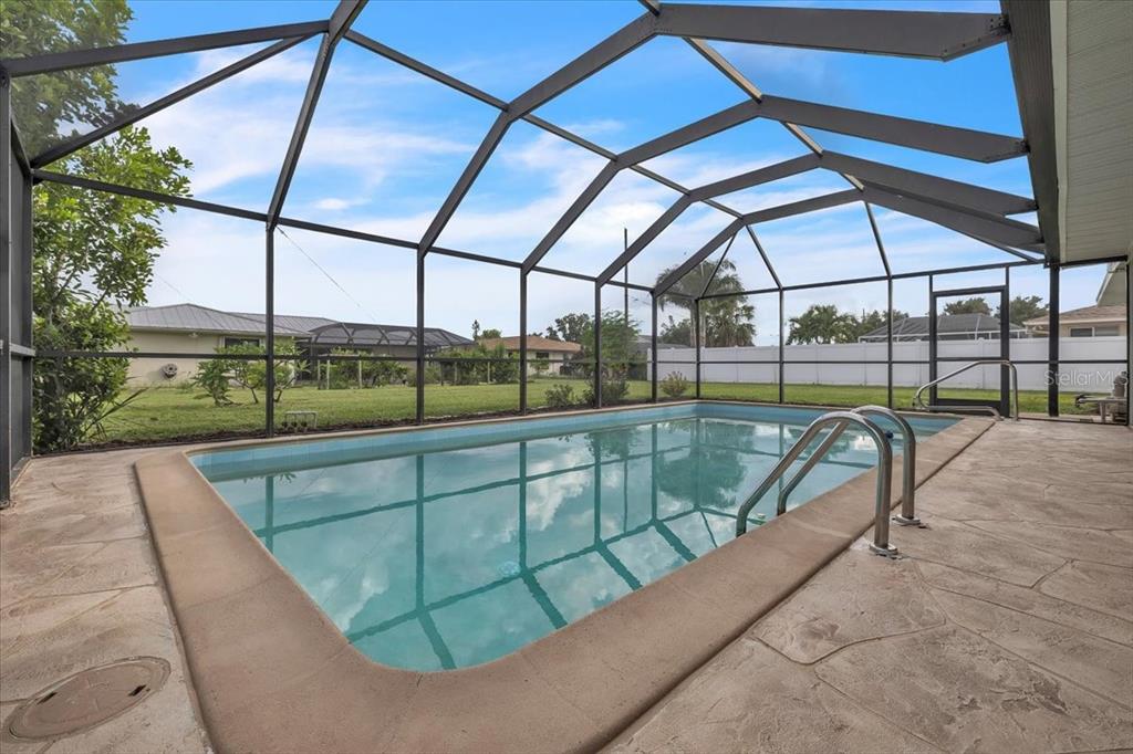 A rectangular swimming pool is enclosed by a screened lanai with a concrete patio — 907 SIDNEY TERRACE NW, PORT CHARLOTTE, FL