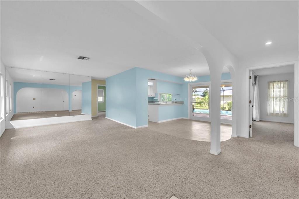 An open-concept living area features light blue walls, beige carpeting, and a mirrored accent wall — 907 SIDNEY TERRACE NW, PORT CHARLOTTE, FL