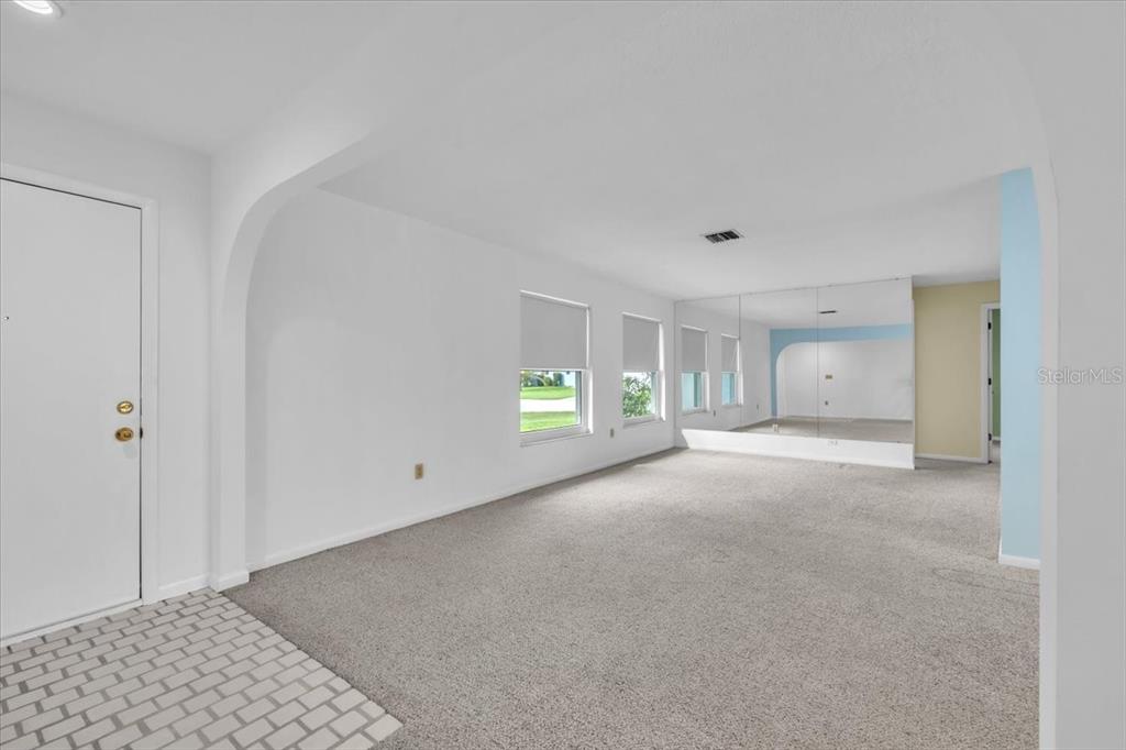 A living room features gray carpeting, white walls, an arched entryway, and a mirrored wall — 907 SIDNEY TERRACE NW, PORT CHARLOTTE, FL