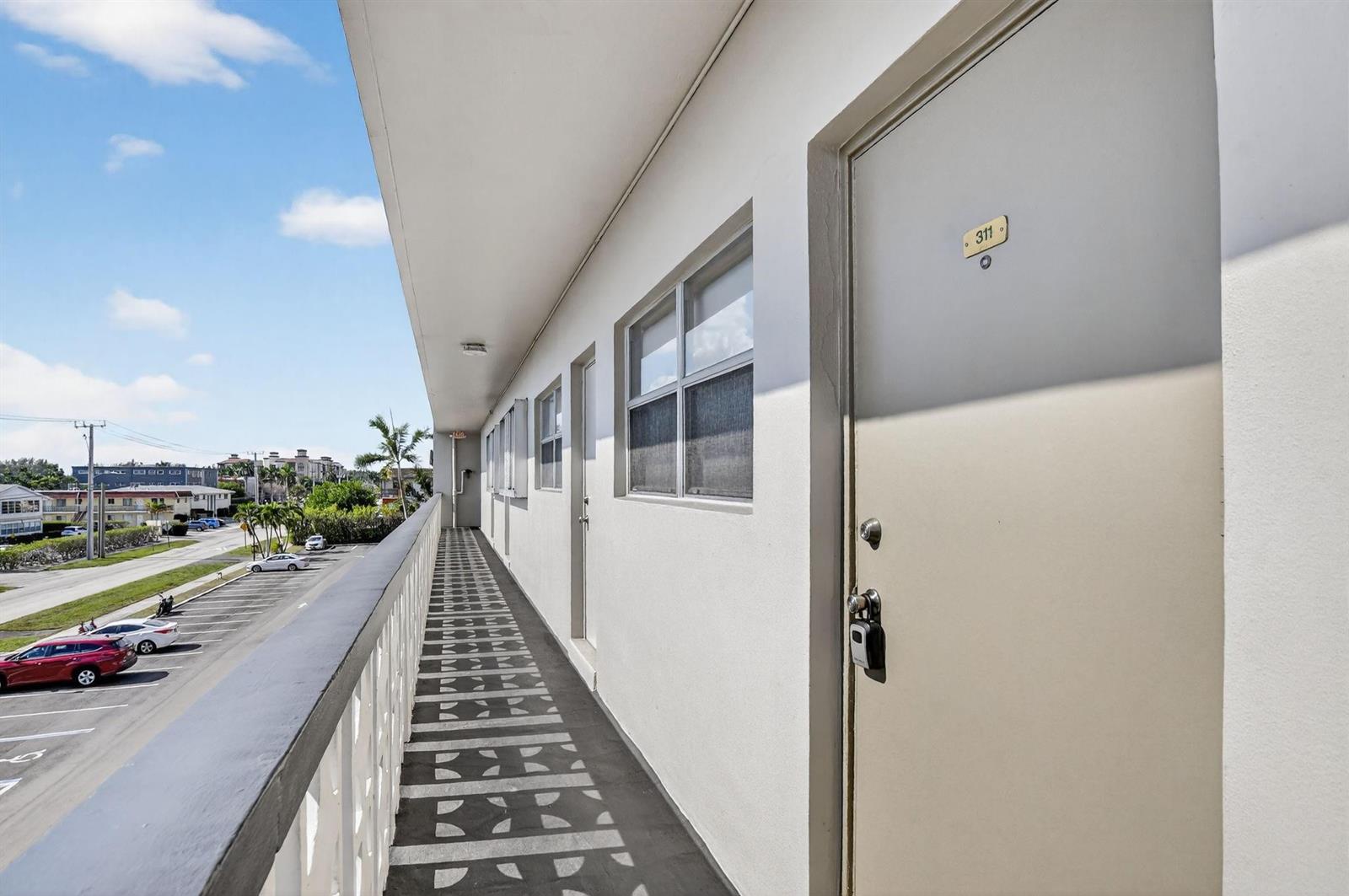 An exterior walkway with a metal railing overlooks a parking lot beside a building — 941 Crystal Lake Drive # 311, Deerfield Beach FL 33064, DEERFIELD BEACH, FL