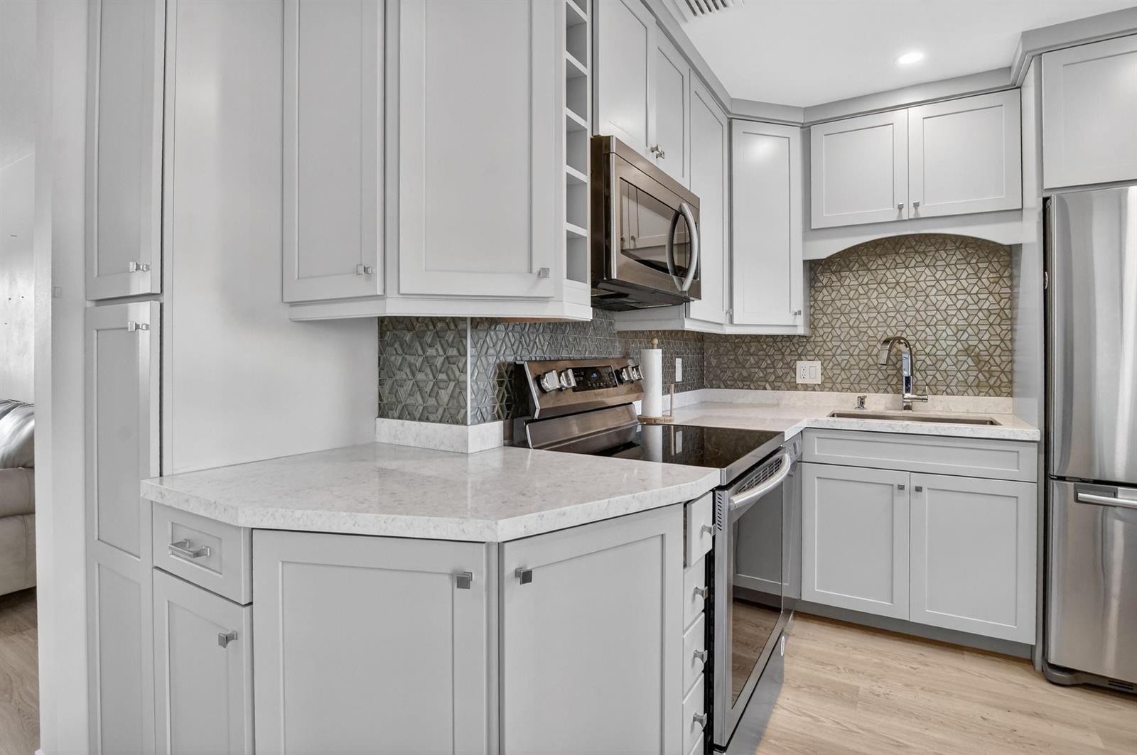 A kitchen features light gray cabinets, stainless steel appliances, quartz countertops, and a geometric backsplash — 941 Crystal Lake Drive # 311, Deerfield Beach FL 33064, DEERFIELD BEACH, FL