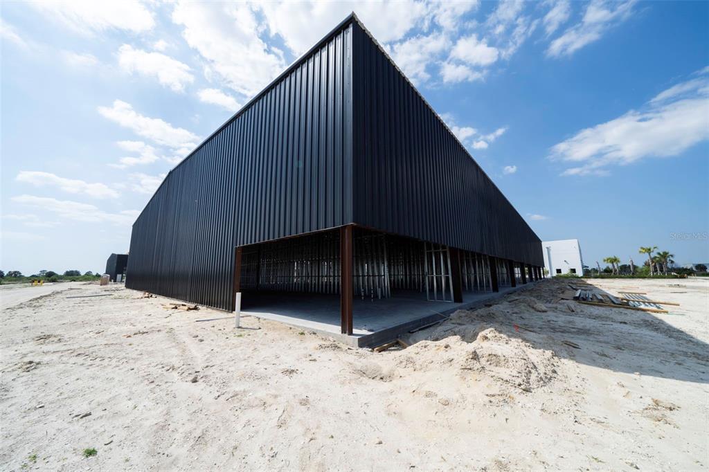 An exterior view of a modern, black metal-sided commercial building under construction on a sandy lot — 8411-8419 DUFFIE DRIVE, PUNTA GORDA, FL