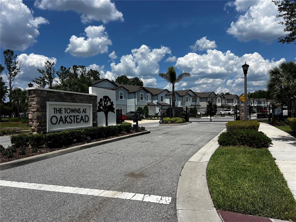 The entrance to The Towns at Oakstead features a stone sign and a gated driveway — 2966 DEER PINE TRAIL, LAND O LAKES, FL