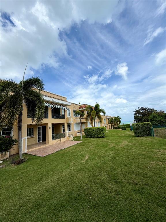 A multi-story tan apartment building with balconies overlooks a large green lawn and palm trees — 968 COSTA DORADA UNIT 101, RIO GRANDE, PR