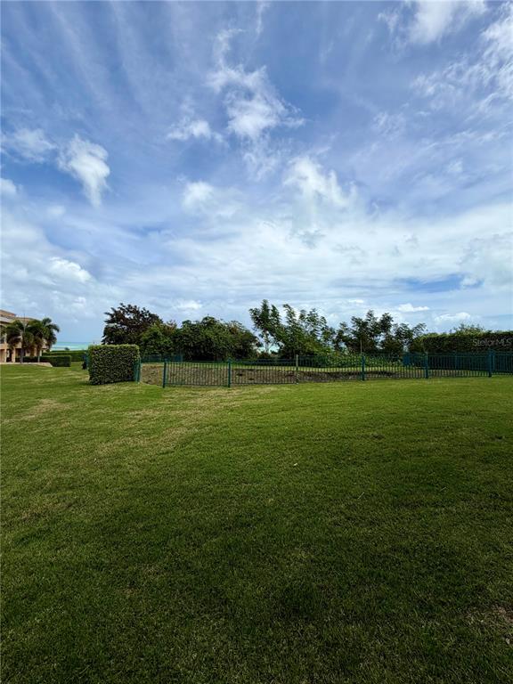 A grassy lawn leads to a fenced area with trees under a cloudy blue sky — 968 COSTA DORADA UNIT 101, RIO GRANDE, PR