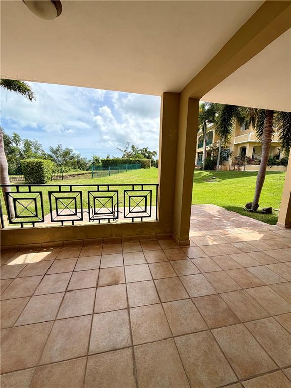 A covered patio with tiled flooring overlooks a grassy lawn and a neighboring building — 968 COSTA DORADA UNIT 101, RIO GRANDE, PR