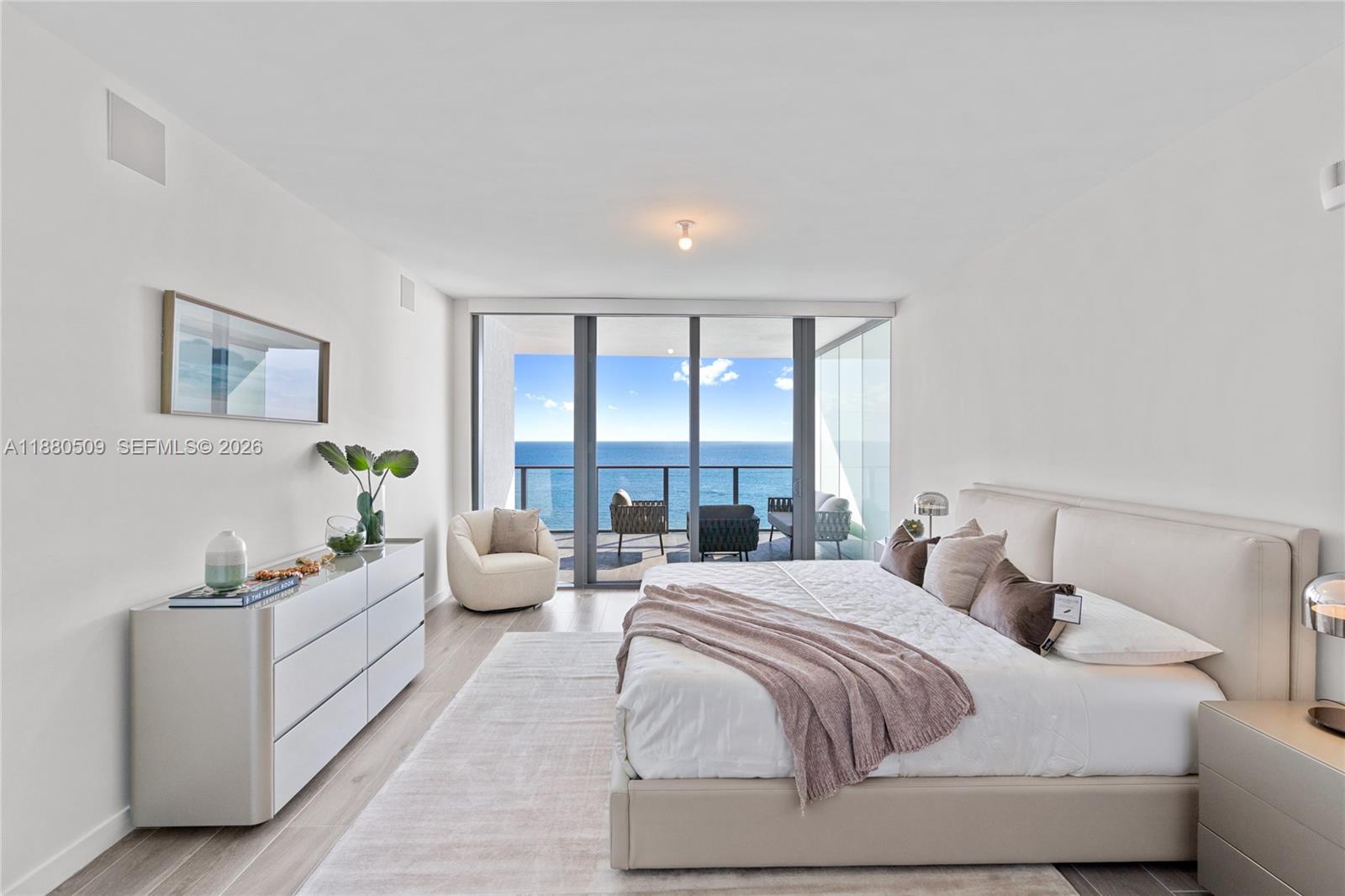 A modern bedroom features a king bed, white dresser, and floor-to-ceiling windows overlooking the ocean — 1116 N Ocean Blvd # 1404, Pompano Beach FL 33062, POMPANO BEACH, FL