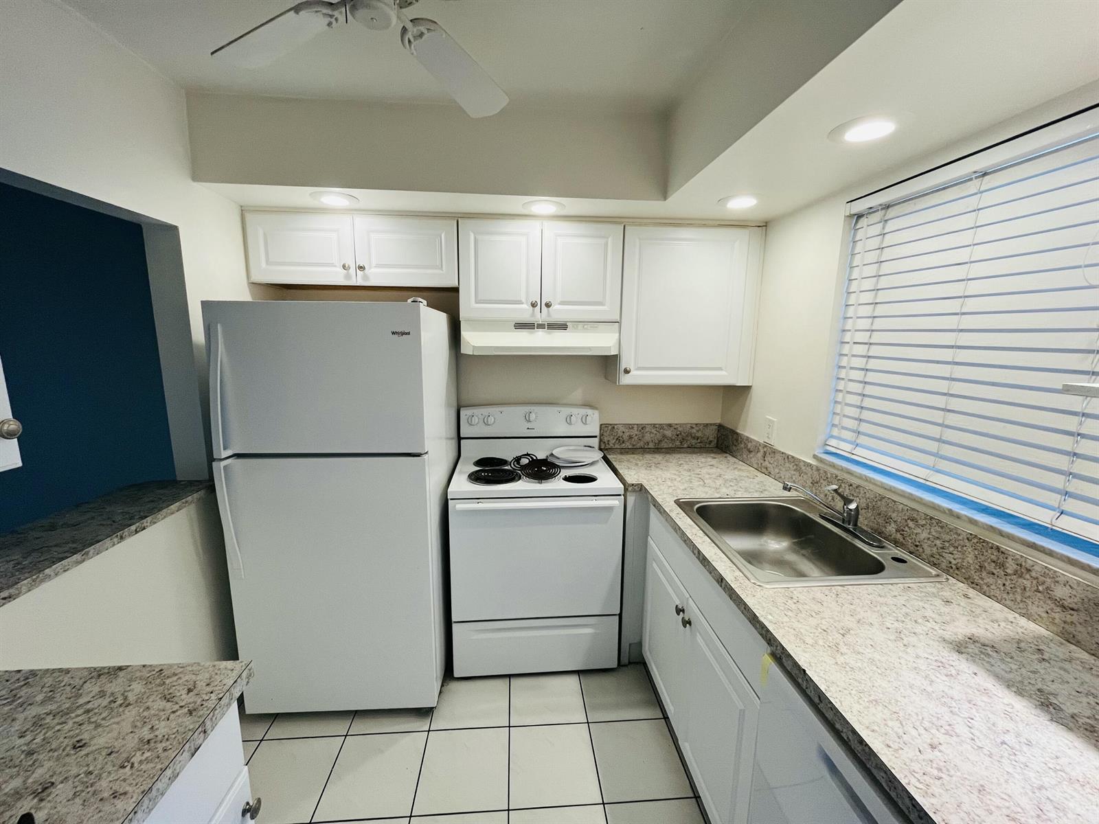 A kitchen features white appliances, white cabinets, and speckled countertops with a tile floor — 9911 Sandalfoot Boulevard # 112, Boca Raton FL 33428, BOCA RATON, FL